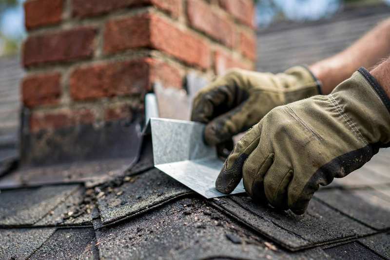 Roofer installing new step flashing where a chimney meets a shingle roof in Sicklerville, NJ